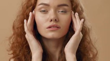 Kıvırcık saçlı genç bir kadın stres belirtileri gösterir, nazikçe başını tutar. İfadesi, sağlam ve sıcak bir arkaplana karşı bir anlık düşüncelere ya da rahatsızlığa işaret ediyor..