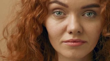 Kıvırcık kızıl saçlı ve yeşil gözlü bir kadın doğrudan izleyiciye bakıyor, doğal güzelliğini iyi aydınlatılmış bir iç mekan ortamında sergiliyor. Yüzü sakin ve davetkar..