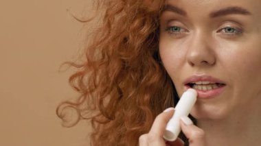 Kıvırcık kızıl saçlı bir kadın aynaya bakarken dudaklarına merhem sürüyor. Tarafsız bir arka planı olan hafif ışıklı bir odada güne hazırlanıyor..