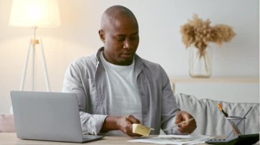 30 'lu yaşlarda Afro-Amerikalı bir adam şık bir ev ofisinde masa başında oturuyor. Çağdaş bir yaşam tarzını somutlaştırmak için finansal meselelere odaklanırken nakit sayıyor..