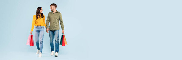 Расслабленная и счастливая пара, наслаждающаяся покупками, держась за руки и неся красочные сумки, воплощая беззаботный и довольный опыт розничной торговли на успокаивающем синем фоне, копировальное пространство