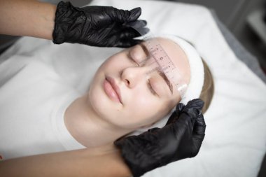 Müşteriye kuaförde kalıcı makyaj prosedürü uygulanır. Bir teknisyen hassasiyet ve konfor sağlarken dikkatlice makyaj yapar. Atmosfer sakin ve güzelliğe odaklı..