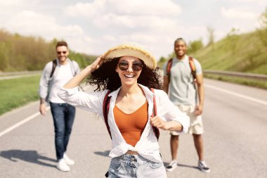 Güzel genç bir kadın erkek arkadaşlarıyla otobanda yürüyor, yaz seyahati yapıyor, sırt çantasıyla dışarı çıkıyor. Otostop, otostop, yaz macerası ve turizm konsepti