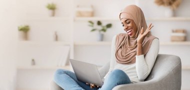 Uzaktan iletişim. Keyifli İslamcı kadın evde dizüstü bilgisayarla video görüşmesi yapıyor, neşeli dindar Afrikalı kadın bilgisayar kamerasına el sallıyor, online toplantıdan keyif alıyor, uzay kopyaları kopyalıyor.