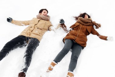 Kış eğlencesi. Karda uzanan, gülen ve el ele tutuşan mutlu çift dışarıda karlı havanın tadını çıkarıyor. Panorama