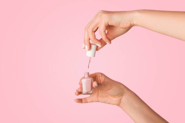 Tanımlanamayan tırnak teknisyenleri pembe arka planda bir şişe cila açıyor, yakın plan. Boş boşluk