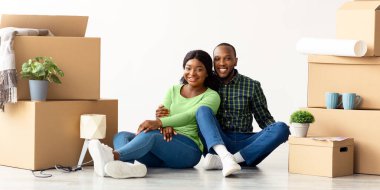 Ev sahibi. New Flat 'e taşınmayı kutlayan mutlu Afrika kökenli Amerikalı çift, Beyaz Oda' da paketleri boşaltılmış karton kutuların arasında oturan neşeli siyah eşler, taşınmanın keyfini çıkarıyorlar, kopyalama alanı