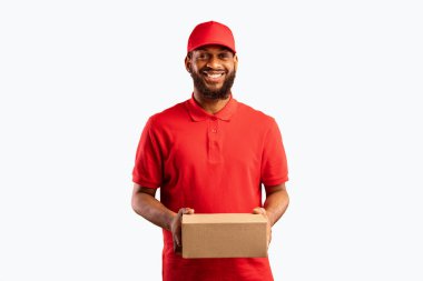 Paket teslimatı. Siyah Kurye, elinde karton kutuyla sarı arka plandaki kameraya gülümsüyor. Stüdyo Çekimi