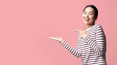 Şuna bir bak. Açık Avuç İçini Gösteren Genç Asyalı Pozitif Kadın Görünmez Nesne Gösteren, Pembe Arkaplanda Poz Verirken Bir Şey Öneren, Boşluğu Kopyalayan Koreli Kadın