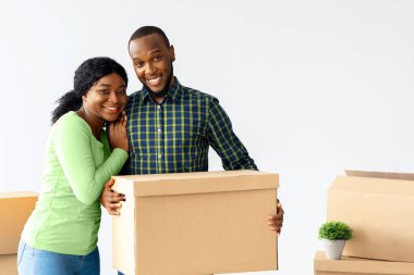 Neşeli genç Afrikalı Amerikalı eşler taşınma gününde karton kutularla poz veriyorlar, mutlu siyah çift yeni evlerine taşınırken, kameraya sarılıp gülümserken,