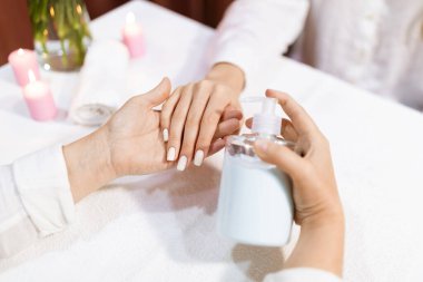 İki kadın şık bir salonda lüks bir manikür deneyimi yaşıyor. Mumlar rahatlatıcı bir atmosfer yaratırken, biri bozulmayı arttırmak için losyon sürüyor..