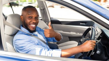 Harika araba. Afro-Amerikalı Mutlu Afro-Amerikalı Adam İşaret İşaretini Gösteriyor, Yeni Otomobil Mağazasında Modern Araç Satıyor veya Tatilin keyfini çıkarıyor, Pencereden Dışarı Bakıyor. Seçici Odaklanma