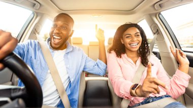 Yol Yolculuğu Konsepti. Heyecanlı Afro-Amerikan çiftin ön manzara portresi. Lüks araba sürüyorlar, müzik eşliğinde dans ediyorlar ve favori şarkılarını söylüyorlar, hafta sonları dinleniyorlar, tatile gidiyorlar, güneş parlıyor.