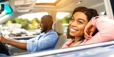 Seyahat kavramının tadını çıkarıyorum. Gülümseyen, Afro-Amerikan bir adam araba kullanıyor, ön koltukta oturan ve pencereden dışarı bakan mutlu ve güzel bir kadına odaklanıyor.