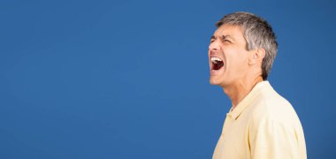 A middle aged man in his 50s yells out in frustration while standing alone against a vibrant blue background, conveying a sense of isolation and emotional intensity, copy space clipart