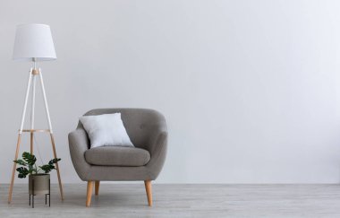 Ev ofisinin, oturma odasının ya da yatak odasının modern minimal iç mekanı. Beyaz yastıklı gri eski bir koltuk, yeşil saksı bitkisi, ahşap zeminde lamba, ışık duvarı arka planında, düz zemin, kopyalama alanı
