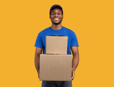 En iyi servis konsepti. Mavi şapkalı gülümseyen siyah teslimatçı ve elinde turuncu stüdyo arka planında izole edilmiş karton kutular tutan biçimsiz adam. Afro-Amerikan kurye paketleri taşıyor.