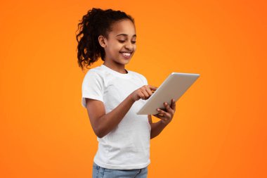 E-öğrenme kavramı. Gülümseyen Afrikalı Amerikalı genç kızın portresi sarı turuncu stüdyo arka planında dijital tablet kullanıyor ve internette geziniyor. Uzak Eğitim