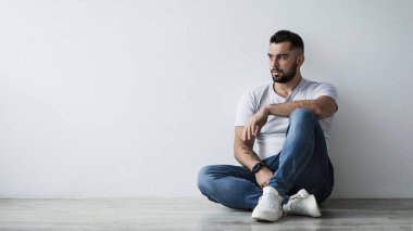 Yalnız yakışıklı adam üzgün, kendini izole etme stresi, agorafobi, depresyon. Milenyum çağından kalma çekici, kaslı bir adam gri duvarda oturuyor ve boş bir alana bakıyor.