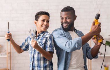 Baba ve Oğul aktiviteleri. Neşeli Afro Çocuk ve babasının elinde inşaat aletleriyle sırt sırta durduğu portre.