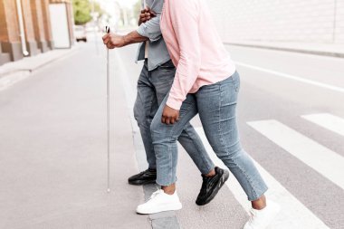 Tanımlanamayan genç siyahi kadın görüş engelli bir adama yardım ediyor. Şehir caddesini geçip, kopyalama alanı yaratıyor. Kör Afrikalı Amerikalı adam ve rehberi yaya geçidini birlikte kullanıyorlar.