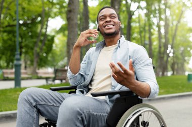 Yeşil Park 'ta tekerlekli sandalyedeki neşeli engelli adam akıllı telefondan konuşuyor. Dışarda arkadaşlarıyla ya da aileleriyle telefon görüşmesi yapan engelli bir gencin portresi