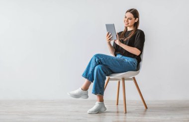 Dijital tabletli neşeli genç bir kadının tam boy portresi beyaz stüdyo duvarına karşı internette çalışıyor. Modern teknoloji ve iletişim kavramı