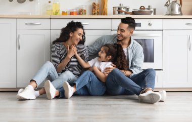 Güzel bir ortadoğu aile babası, anne ve kızı rahat beyaz bir mutfakta yerde oturuyor, sevgi dolu ebeveynler sevimli küçük çocuklarıyla vakit geçiriyorlar, sohbet ediyorlar, gülüyorlar, boşlukları kopyalıyorlar.