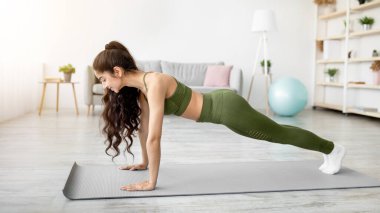 Binlerce yıllık Hintli kadının yoga minderinin üzerinde tahta duruşu, panorama. Zinde Doğulu kadın güç egzersizi yapıyor, Coronavirus karantinası sırasında aktif yaşam tarzı yönetiyor.