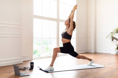 Atletik Genç Kadın Başının üstünde Silahlarla İleri Antrenman Yapıyor Evde Antrenman İzliyor, Yoga Mat 'te Bir Savaşçı Pozu Veriyor. Yurtiçi Kadın Fitness Konsepti