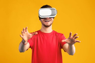 Siberuzay ve Gelecek Teknoloji Konsepti. Sanal gerçeklik deneyimi sırasında VR kulaklık takan gülümseyen adam havaya dokunuyor. Mutlu sakallı adam yapay bilgisayar dünyasını keşfediyor, mavi stüdyo duvarı