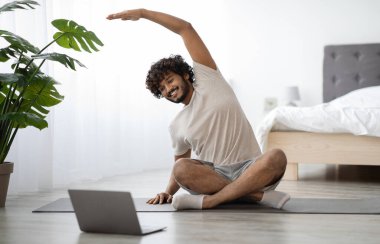 Binlerce yıllık Hintli tişörtlü ve şortlu adam yoga minderinde oturuyor, dizüstü bilgisayara bakıyor ve esniyor, sabahları fitness dersi alıyor, yatak odasının içi, fotokopi odası...