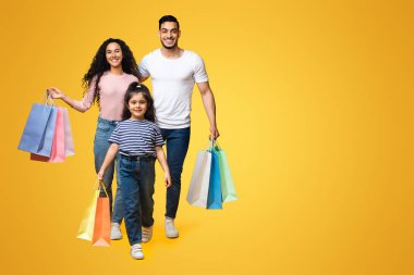 Alışveriş günü. Parlak alışveriş torbalarıyla stüdyoda gezen neşeli genç Orta Doğulu aile, mutlu Arap ebeveynler ve kadın çocuk mevsimlik satışlardan keyif alıyor, kopyalama alanı.