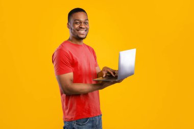 Serbest meslek hayatı. Sarı Arkaplan 'ın üstünde duran Stüdyo Çekimi' ne gülümseyen dizüstü bilgisayar kullanan mutlu siyah adam. İnsan ve Gadget 'lar, E-Öğrenme ve İnternet Teknolojileri Konsepti