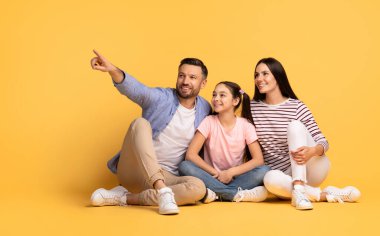 Bir baba, anne ve kızları birlikte parlak sarı bir arka planda oturup gülümsüyor ve neşeli bir anı paylaşıyorlar. Yakınlıkları ve yakınlıkları güçlü aile bağlarını vurguluyor..
