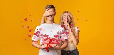 Bir çift sevinçli ve sürpriz bir anın tadını çıkarırken, bir partner diğerinin gözlerini şakayla örtüyor. Renkli kalpler arka planı doldurur, paylaştıkları sevgi ve sevgiyi arttırır..