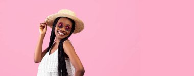 Afro demetli oyuncu zenci kadın pembe stüdyo arka planında boş alana bakıyor, panorama. Moda kıyafetli, poz veren ve gülümseyen Afrikalı Amerikalı genç bir kadının portresi.