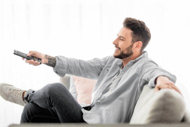 Rahat adam evde televizyon izlerken uzaktan kumandayla kanal değiştiriyor, oturma odasında dinleniyor, hafta sonu eğlencesinin tadını çıkarıyor, kopyalama alanı, yan görüş