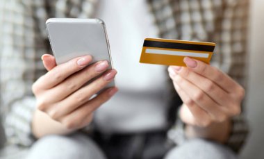 Modern cep telefonu ve kredi kartı tutan, evde otururken mal ve hizmetlere ödeme yapan, internet üzerinden alışveriş için mobil uygulama kullanan, kapalı çekim yapan bir kadın. E-ticaret, online bankacılık