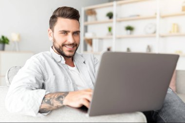 Kanepede dizüstü bilgisayarı, panoraması, fotokopisi olan olumlu bir adam. Yakışıklı adam defter kullanıyor, film izliyor, internette sörf yapıyor ya da sosyal ağlarda geziniyor.