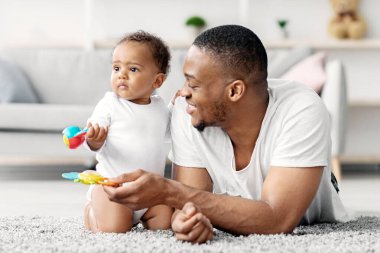 Mutlu Afrika kökenli Amerikalı baba, evde küçük bir çocukla oynuyor, küçük siyah babayla ilgileniyor, küçük bebek oğluyla oturma odasında vakit geçiriyor, oyuncakları kullanıyor ve yakınlaşıyor.