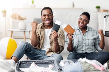 Tatil, sonunda. Neşeli Afrika kökenli Amerikalı çift, ellerinde seyahat biletleri ile evde bavullarıyla oturan kameraya gülümsüyor. Yeni Gezimizi Kutlayan Mutlu Turistler. Seçici Odaklanma