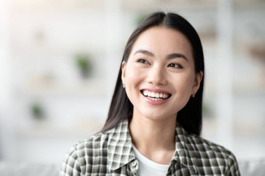Evdeki koltukta oturan neşeli Asyalı genç bayan fotokopi odasına bakıyor ve gülümsüyor. Güzel Koreli kadın rahat bir oturma odasında kanepede dinleniyor, boş bir yere bakıyor, hafta sonunu yalnız geçiriyor.