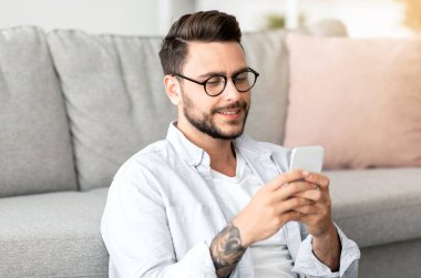 Kullanışlı bir uygulama. Yakışıklı milenyum adamı evde dinlenirken smatphone kullanıyor, yerde oturuyor oturma odasında kanepeye yaslanıyor, fotokopi çekiyor. İnternette gezinen ya da arkadaşlarıyla mesajlaşan adam