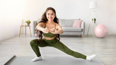 Kilitlenme ev antrenmanı. Oturma odasında yoga minderinin üzerinde bacaklarını esneten genç, sportif Hintli bir bayan. Pozitif Doğulu kadın esneklik egzersizleri yapıyor, formda ve sağlıklı kalıyor, eğitimden zevk alıyor.