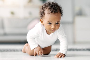Evinde yerde sürünen sevimli, küçük siyah bebek portresi, sevimli, Afro-Amerikan bebek giysisi giyen, oturma odasını keşfeden, seçici odak, serbest alan