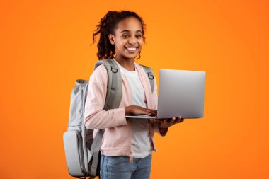 Sırt çantasıyla gezen, klavyeye yazı yazan, sarı stüdyo arkasında izole bir şekilde duran gülümseyen Afrikalı Amerikalı kızın portresi.