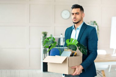 Ekonomik kriz konsepti. Ofiste kovulduktan sonra kişisel eşyalarını elinde tutan mutsuz bir Arap. Resmi giyinmiş işsiz bir doğu çocuğu işini kaybettikten sonra depresyona giriyor.