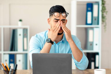 Milenyum Arap çalışanı yorgun, tahriş olmuş gözlerini ovuşturuyor, çok fazla dizüstü bilgisayarla çalışıyor, ofisteki online işten yorgun düşüyor. Genç Doğulu işadamı ekrana bakmaktan yorgun düştü