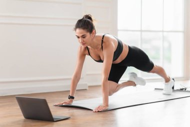 Online Eğitim Konsepti. Dağ tırmanışçıları egzersizi yapan, video dersi izleyen ya da bilgisayar dersine giren, ekrana bakan, geniş apartmanında egzersiz yapan odaklanmış bir bayan.